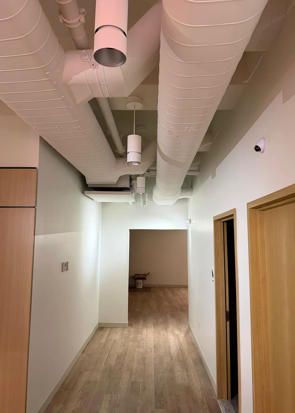 Finished commercial corridor with exposed white ductwork and wood door details